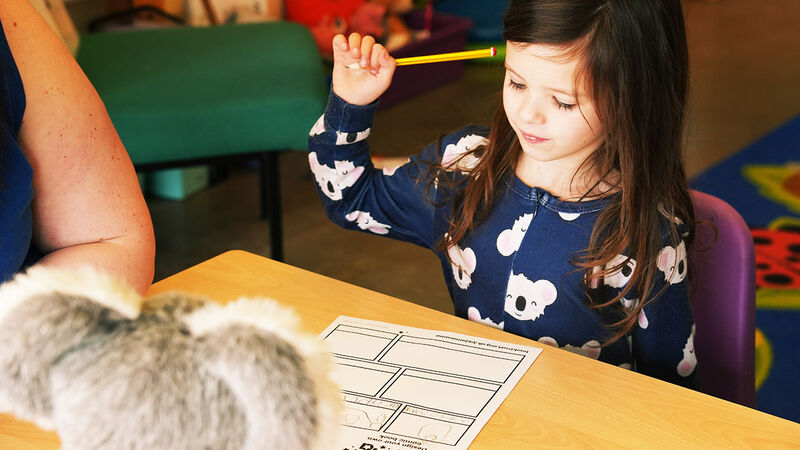 A girl thinking about how to fill in a Pyjamarama activity sheet, holding up her pencil