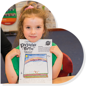 A girl smiling while holding up a Pyjamarama activity sheet she has completed