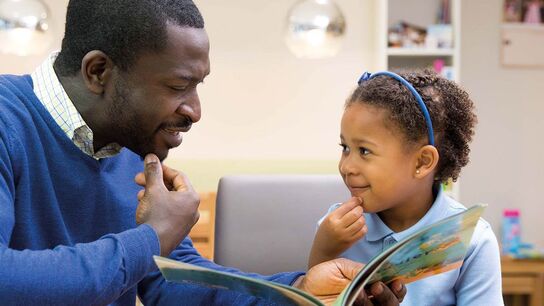 A father reading to his daughter at home.