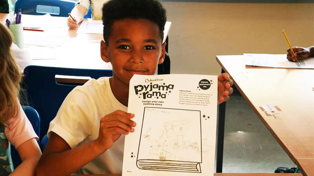A child smiling while holding up a Pyjamarama activity sheet
