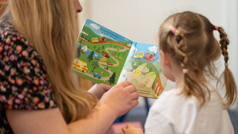 A girl and a woman sharing a book, seen from behind