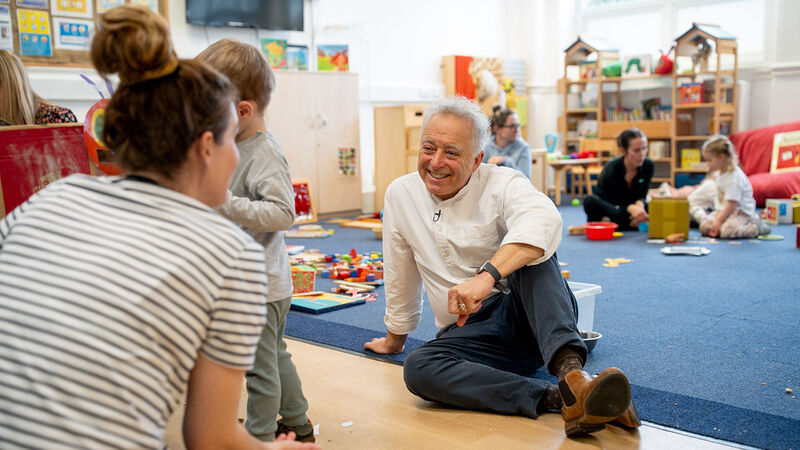 Frank Cottrell-Boyce sitting on the floor at Linaker smiling and speaking to a parent