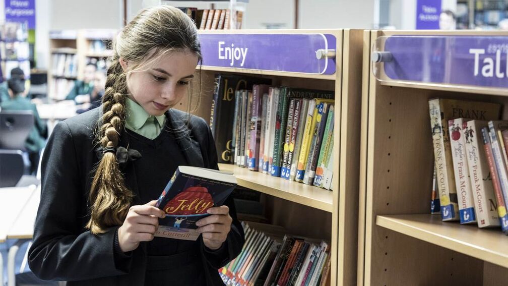A secondary school student in the library looking at the blurb of a book.