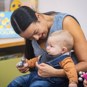 A mother is sitting with a baby on her lap at a Storytime session