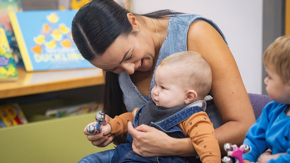 A mother is sitting with a baby on her lap at a Storytime session
