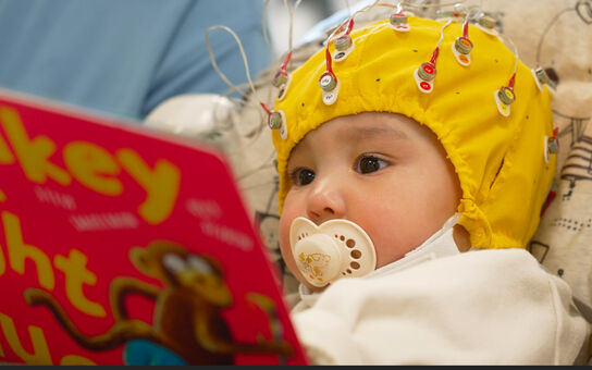 baby reading a book and wearing a cap with sensors to measure brain activity
