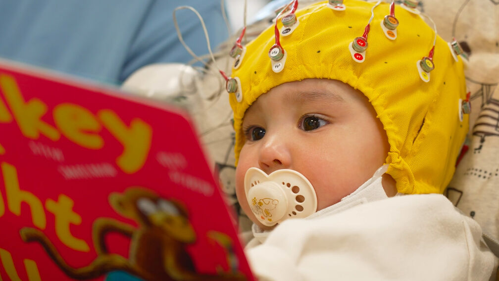 baby reading a book and wearing a cap with sensors to measure brain activity