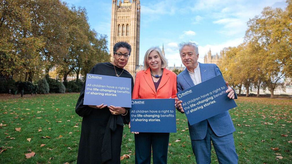 Patrice Lawrence, Diana Gerald and Frank Cottrell-Boyce standing outside the Houses of Parliament holding signs which say 'All children have a right to the life-changing benefits of sharing stories.'