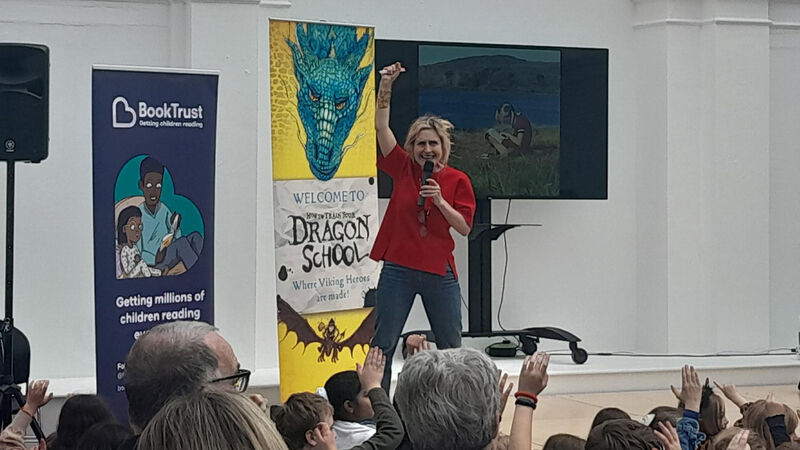 Cressida Cowell with her fist in the air at a Leeds Libraries event sponsored by BookTrust