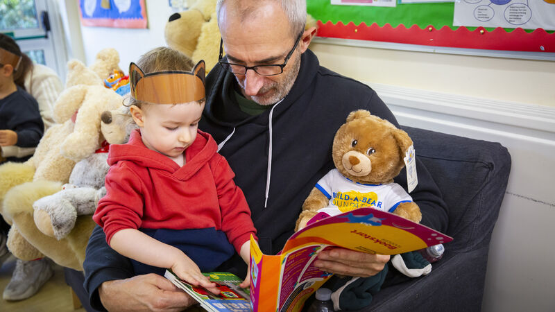 A man, and child and a Build-a-Bear teddy opening up a Bookstart pack in Datchet