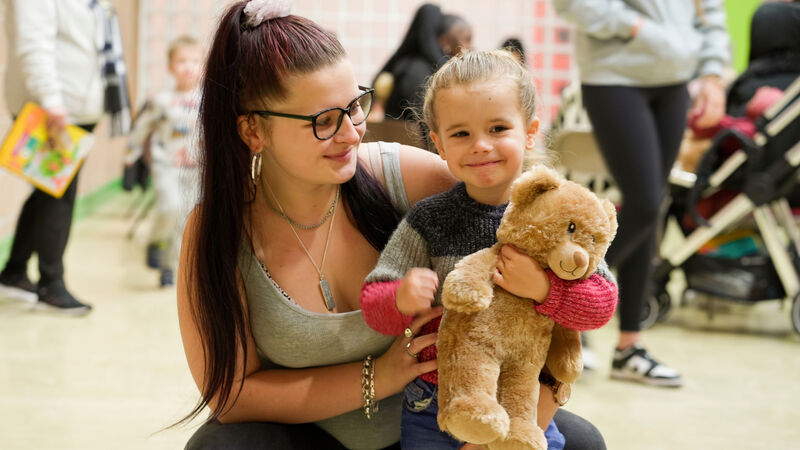 A woman smiling while hugging a child who is holding a Build-a-Bear teddy