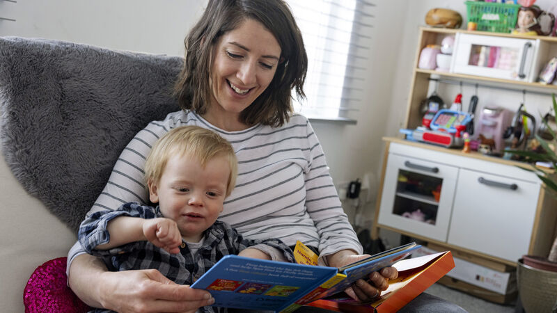 Carer with arm around toddler both looking down and reading a book together