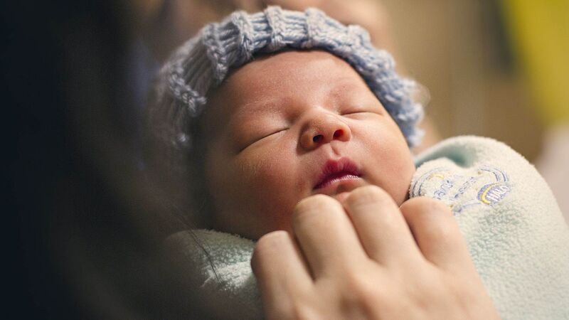 A sleeping baby in a blue woolly hat, being tended to by an adult