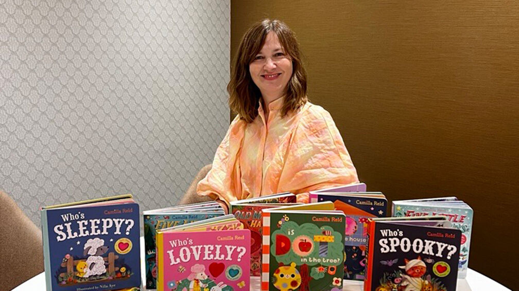 Camilla Reid sitting and smiling behind a table with some of her books on it
