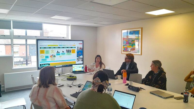 several people sitting at a table in front of a big screen in discussion