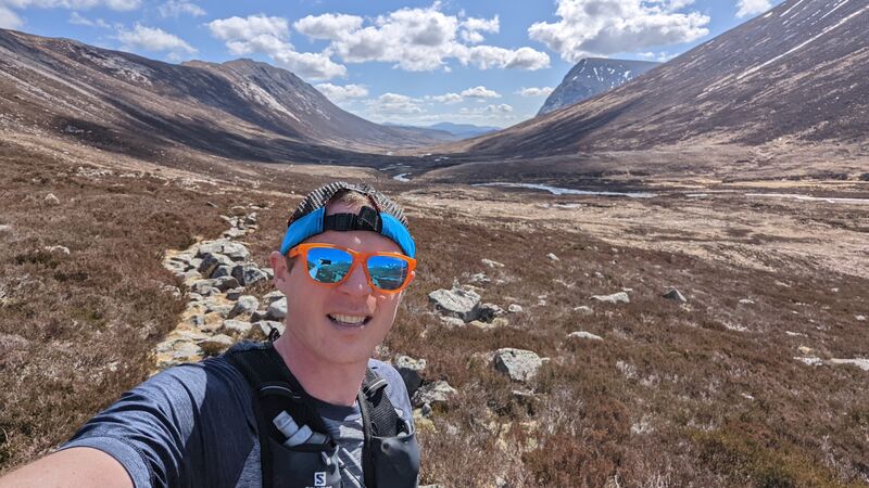 man taking a selfie with sunglasses on with brown hills and ground behind him