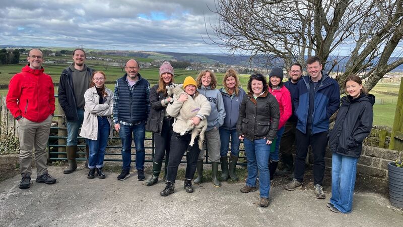 a group of people standing in a row posing for the camera with a green field behind them