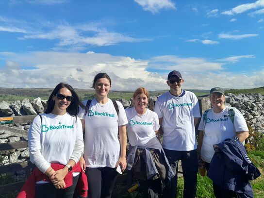 five people wearing white t-shirts facing head on in front of a stone wall in a green field