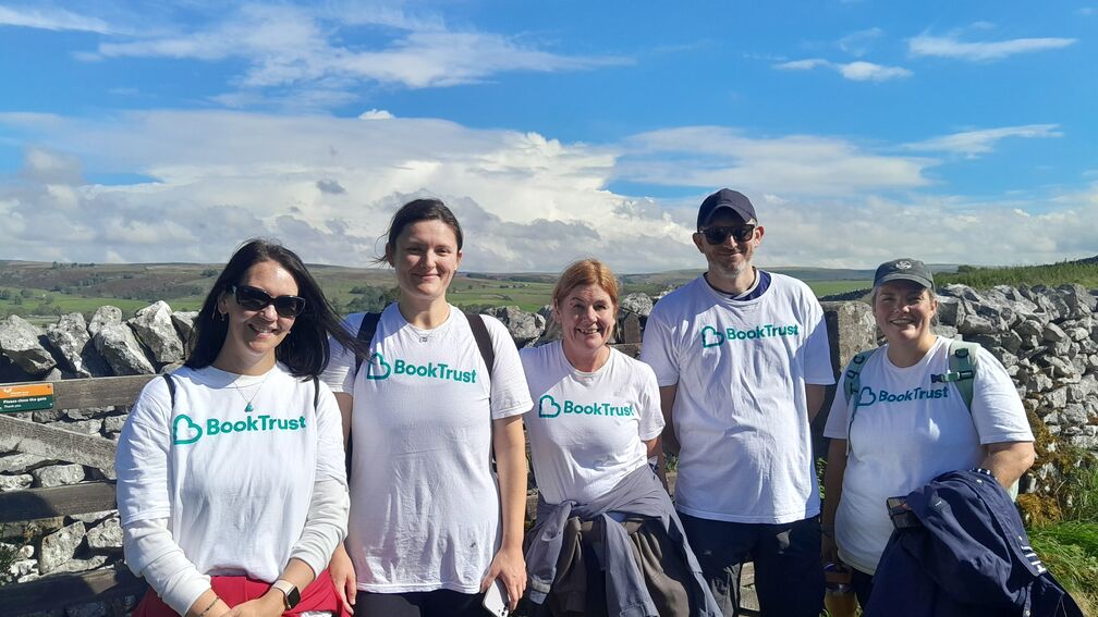 five people wearing white t-shirts facing head on in front of a stone wall in a green field