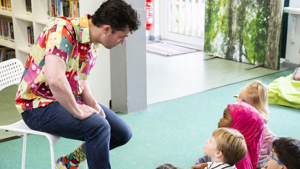 person (Chip colquhoun) sitting on a chair talking to a group of children sitting on the floor