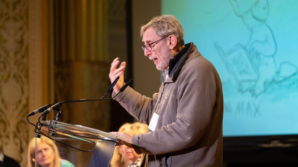 Michael Rosen standing side on giving a speech on stage