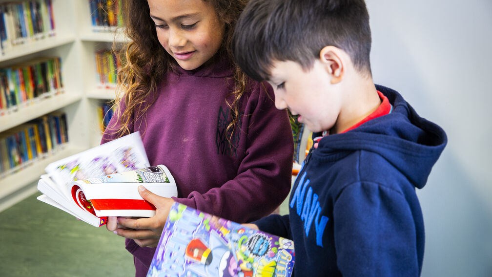 girl and a boy standing up looking at picture books