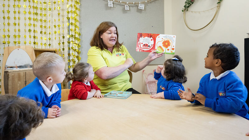 person holding up a book reading aloud with a group of school children all looking at the book