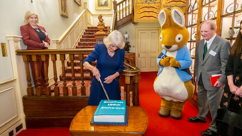 Her Majesty The Queen cuts a BookTrust 100th anniversary cake, watched on by Peter Rabbit wearing a BookTrust sash, Sir Michael Morpurgo, and BookTrust Co-CEO Diana Gerald