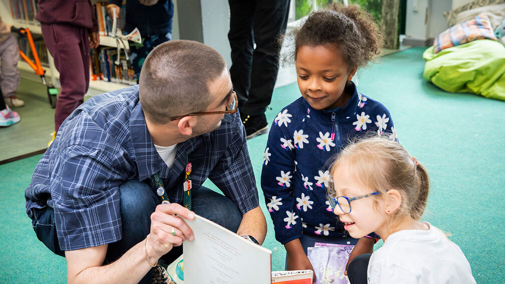 A teaching assistant showing a book to two smiling children