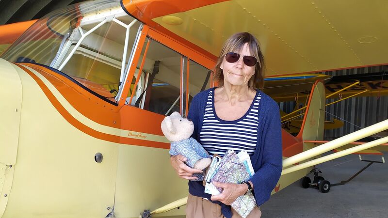 woman standing in front of yellow airplane model holding a teddy bear
