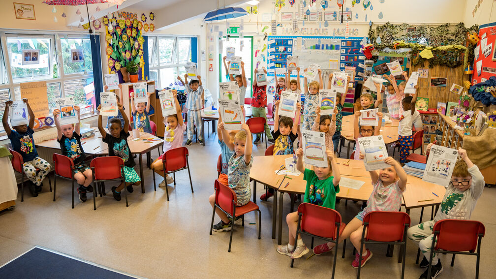 children sitting in a classroom holding up paper certificates