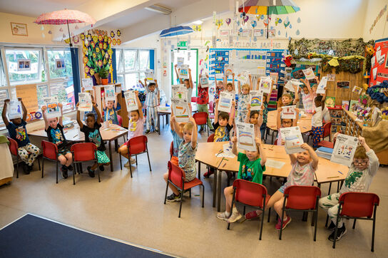 children sitting in a classroom holding up paper certificates