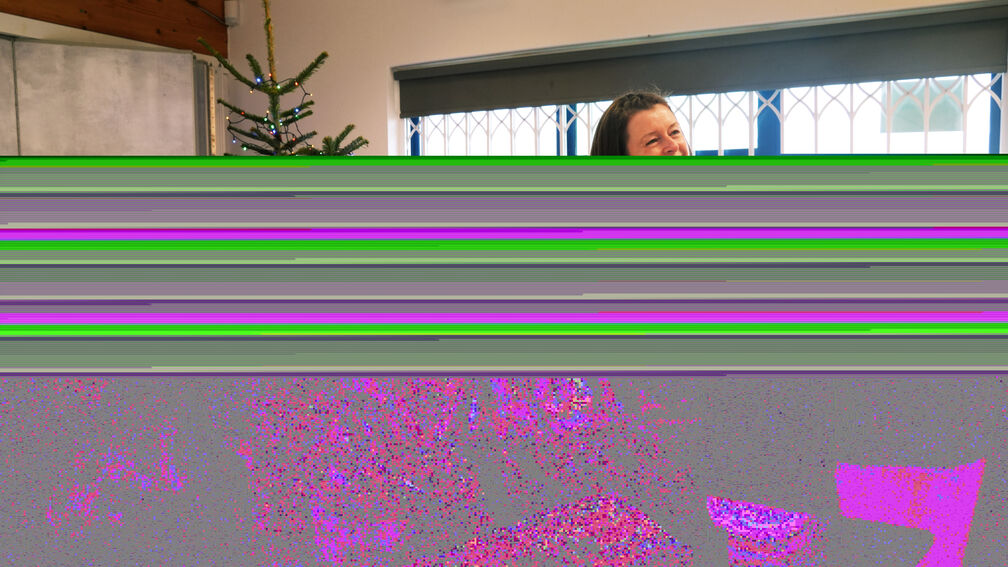 A woman in front of a table piled with food parcels, handing a BookTrust Christmas bookpack to someone not pictured