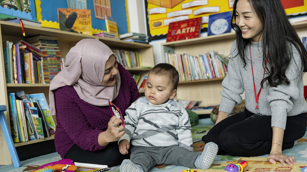 mum and baby sitting on the floor looking at a colourful card along with professional