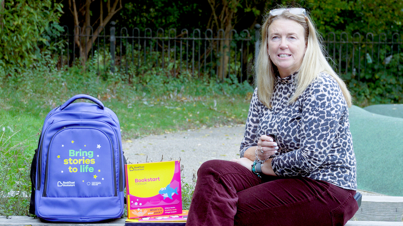 Angela Russell sitting down with blue Bookstart bag and booklet