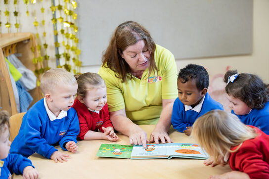 A woman is reading out a picturebook to a group of preschoolers who are interacting with the book and looking interested