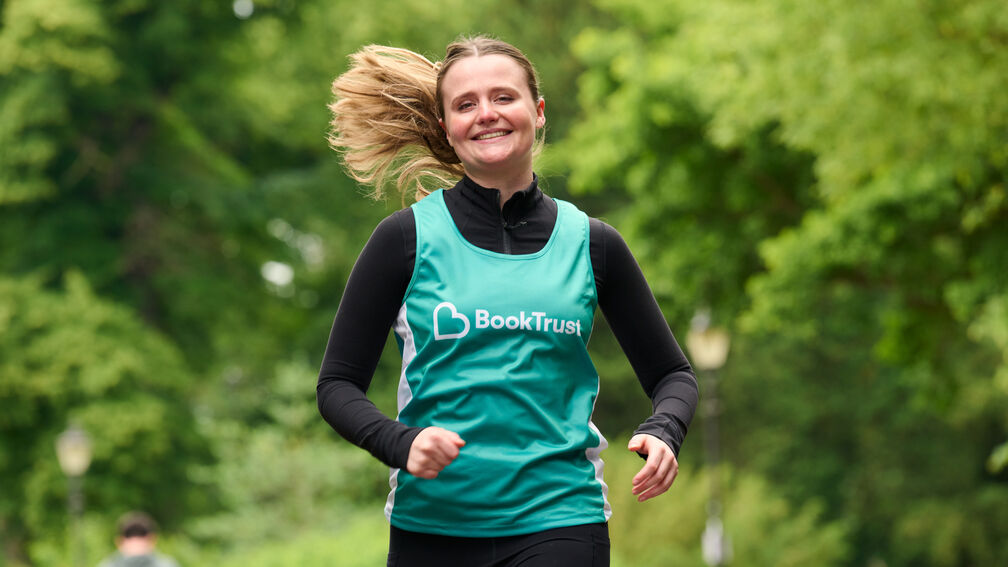 woman smiling and running wearing a teal running vest which has a BookTrust logo on it