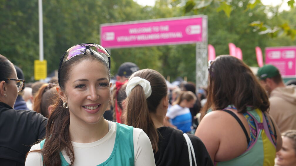 woman standing and smiling at camera with a crowd of supporters and runners behind her at a marathon