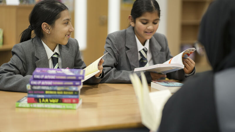 Two secondary school aged girls are sat a table reading together and chatting