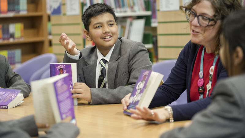 A school librarian is leading a group discussion with some school children, they are all laughing.
