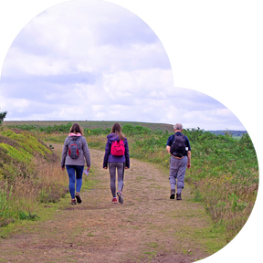 three people with backpacks walking on a dirt path