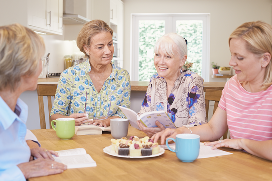group of women at a wooden table in a kitchen hosting a book club