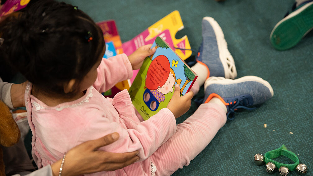 A girl sitting on the floor looking at a book provided by BookTrust with a Bookstart pack next to her