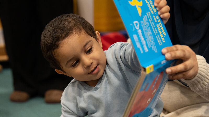 A child smiling while looking at a book being held up by an adult