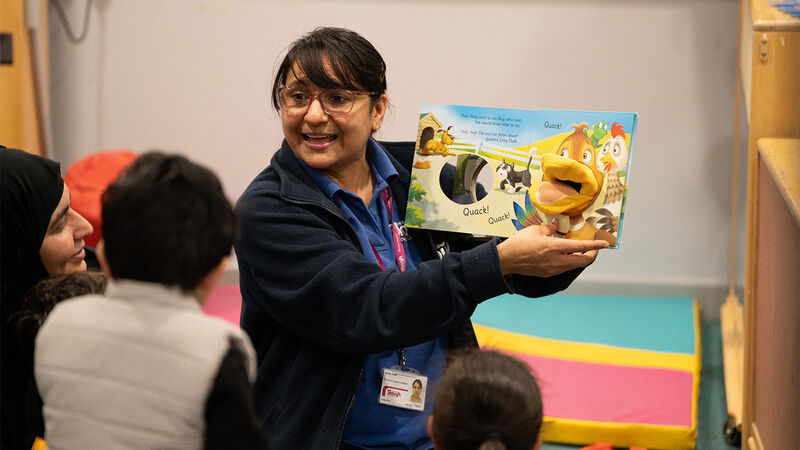 A photo of a practitioner smiling while sharing a book with families