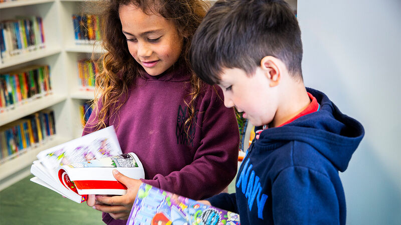 Two children smiling and looking at books