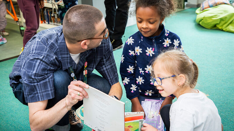 A teacher and two smiling children looking through a book box together