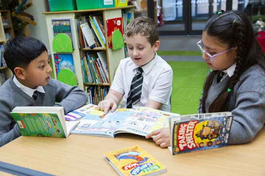 three primary school children sitting at a table discussing books
