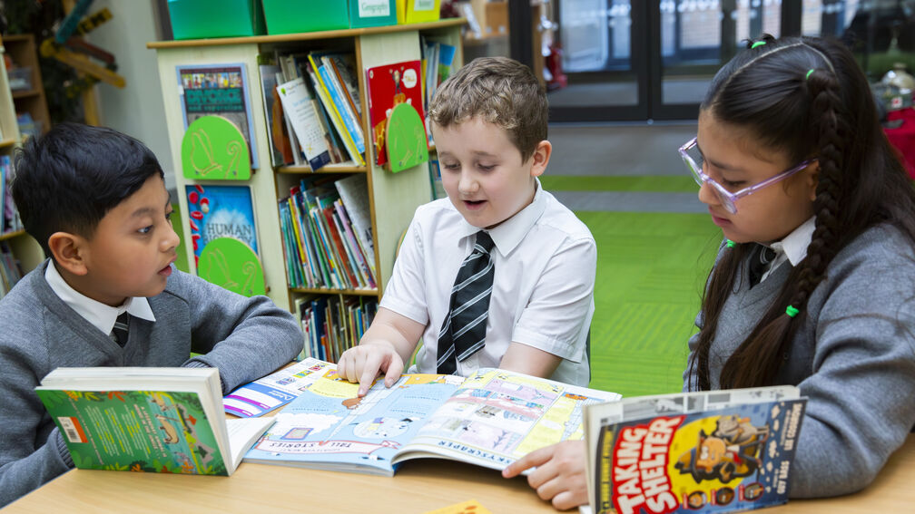 three primary school children sitting at a table discussing books