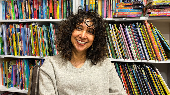 Radha Chakraborty smiling while sitting in front of shelves of children's books